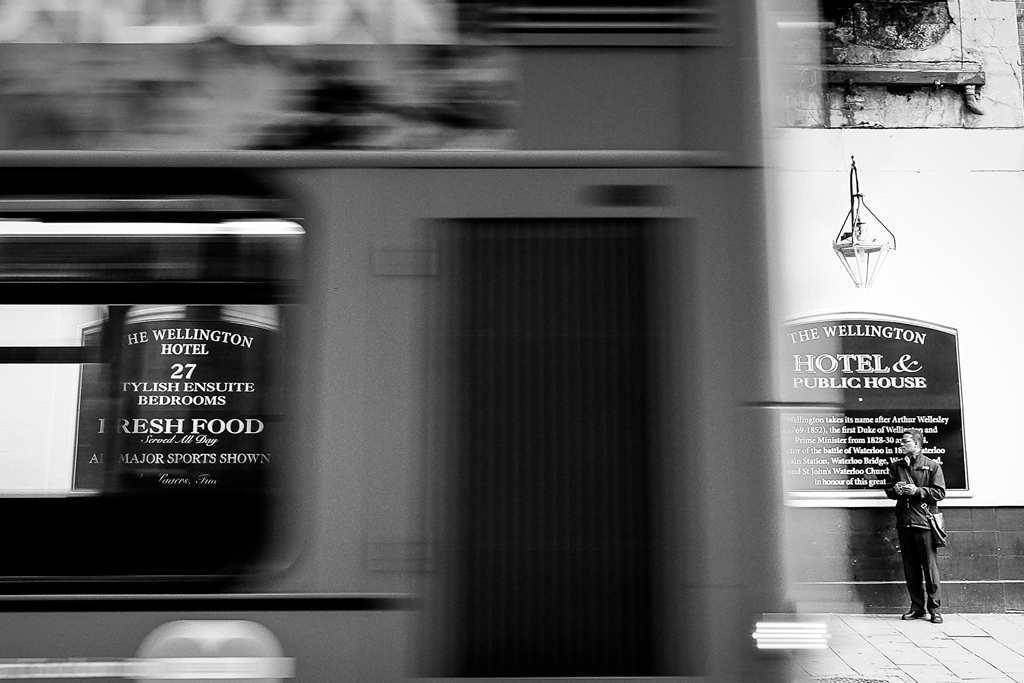 Autobus in movimento davanti al Wellington Hotel con un uomo fermo sul marciapiede