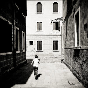 Bambino che corre in un campo veneziano tra luce, ombra e architettura