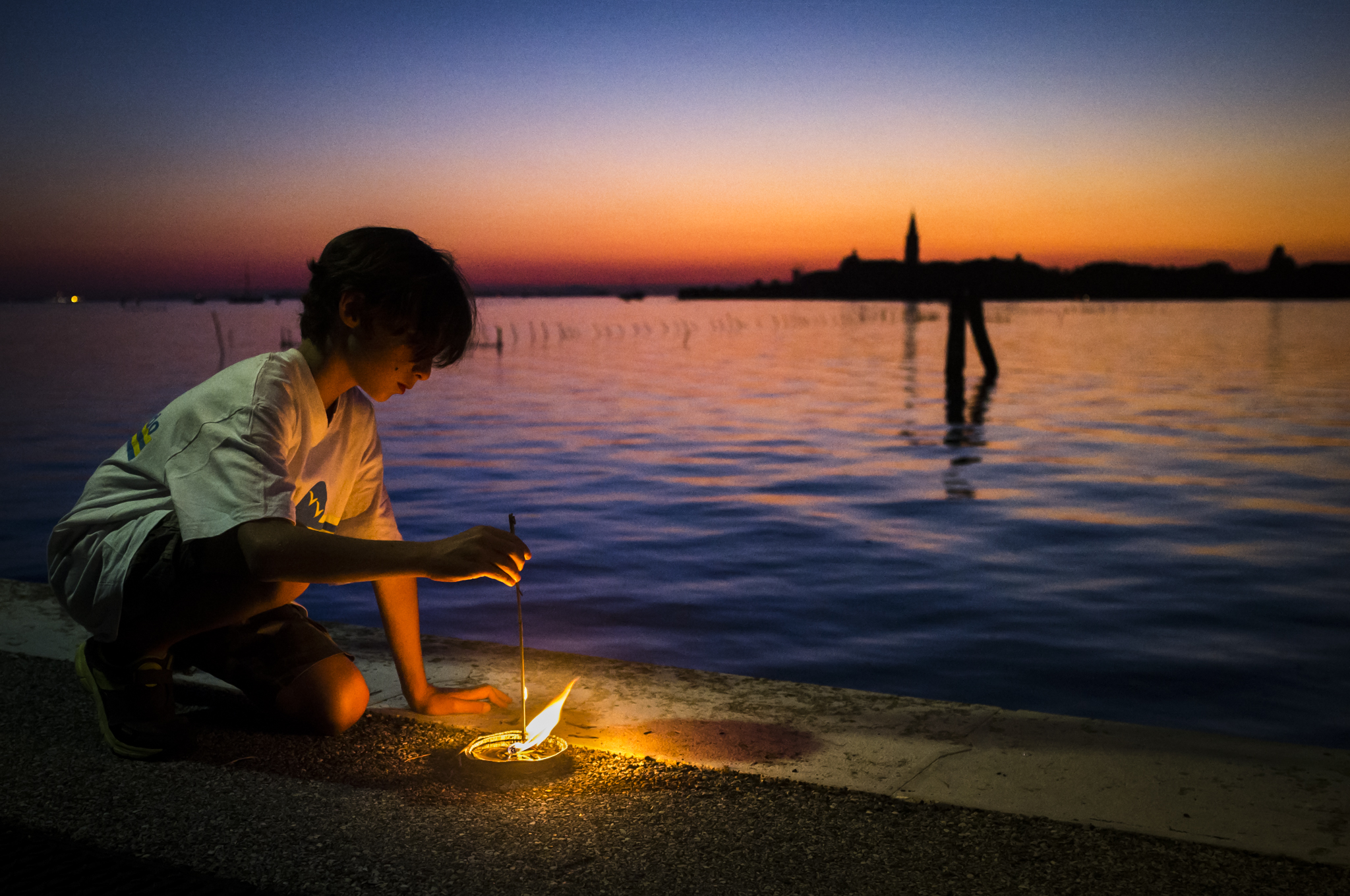 Ragazzo illuminato da una piccola fiamma al tramonto nella laguna veneziana
