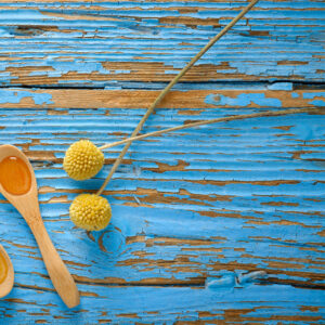 Cucchiaini in legno e piccoli fiori gialli disposti su una superficie di legno azzurro