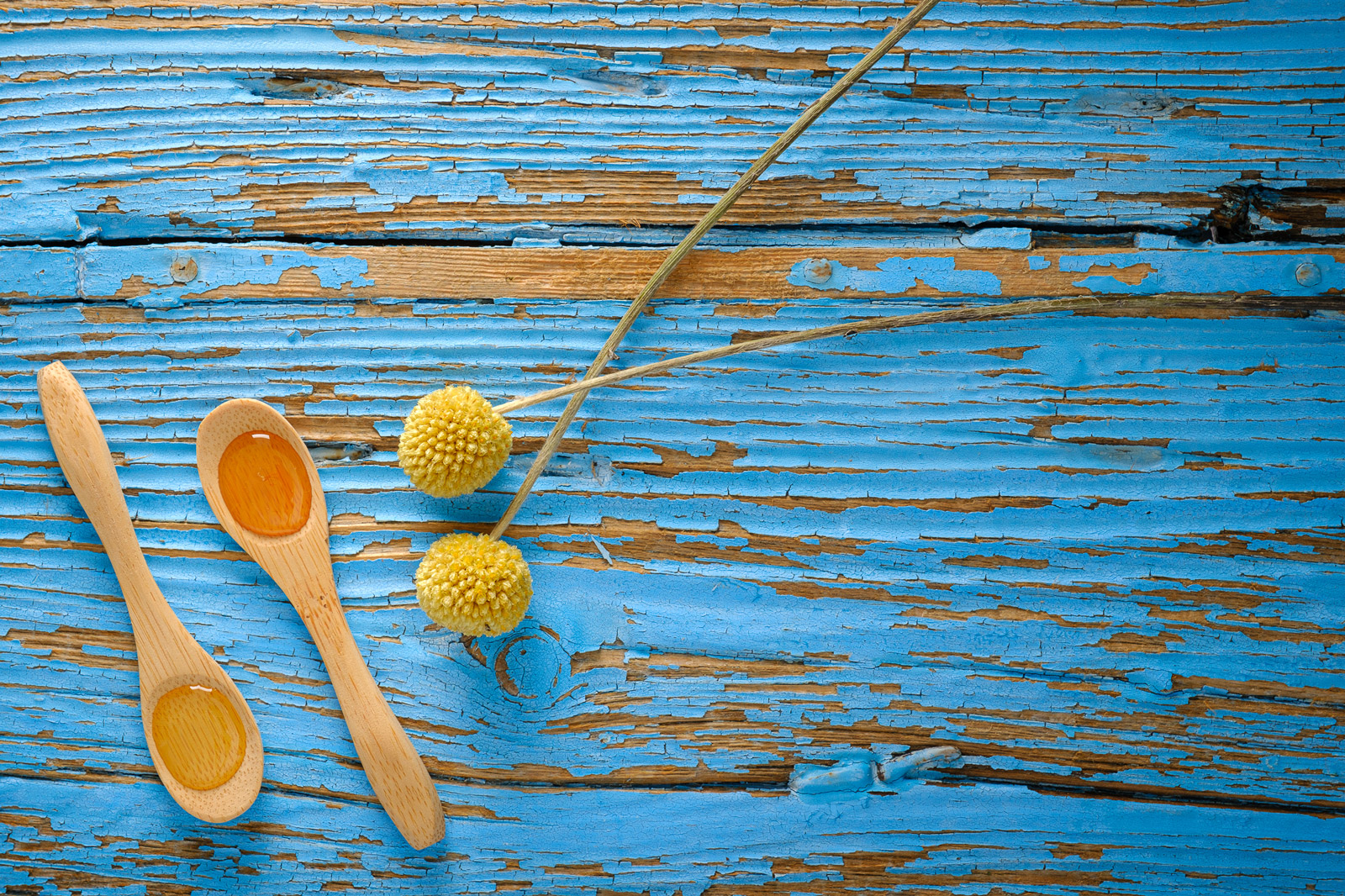 Cucchiaini in legno e piccoli fiori gialli su superficie azzurra