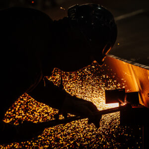 Operaio al lavoro tra scintille e luce arancione in ambiente industriale